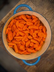 Large pot of sliced chopped and peeled carrots, resting on a wooden table. These vegetables are ready to be cooked up to be a delicious dinner side.