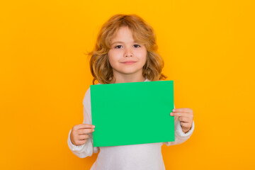 Kid showing empty sheet of paper on yellow background. Portrait of a kid holding a blank placard,...