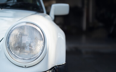 Vintage car close up. Headlamp or head light of white car parked in front of car. . Front view of stylish car. Sportscar background. selective focus. © Petra Richli