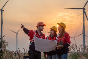 Three people wearing safety gear and pointing at a wind turbine