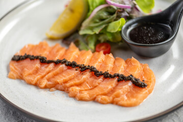 A plate of thinly sliced salmon with a side salad, lemon wedge, and a small dish of dressing.