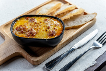 A delicious looking dish of creamy pasta with bread and cutlery on a wooden board.
