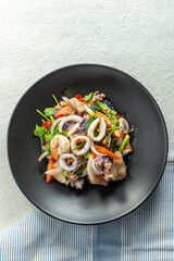 A plate of spicy Thai seafood salad with squid, vegetables and glass noodles.