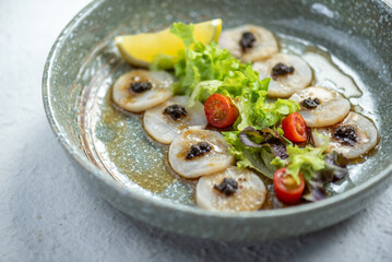 Close-up of a delicious seafood dish with scallops, black olives, cherry tomatoes, and a lime wedge.