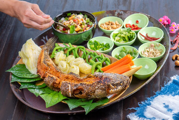 Deep fried fish with fresh vegetables and spicy sauce on a banana leaf.