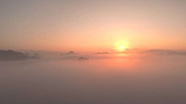 Moving white clouds blue sky scenic aerial view sunrise. Drone flies high back in blue sky through fluffy clouds in morning at orange sun summer. Sun is hidden behind clouds at fog. Nature