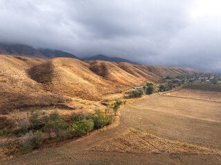 View of autumn landcape with mountains and hills. Large clouds in the sky. Yellow fields in front of the hills. Vivid natural scenery photo.