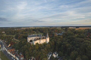 Naklejka premium Majestic castle perched atop a lush hill under a serene sky at sunset near a quaint village