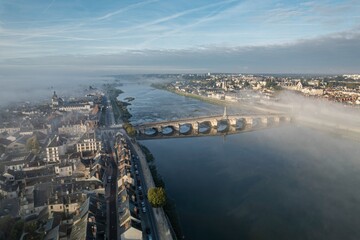 Misty morning view of a serene river flowing through a quaint town surrounded by lush landscapes