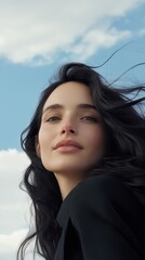 Fototapeta premium Close-up of a young woman looking upwards, with the wind gently blowing her hair against a bright sky background.