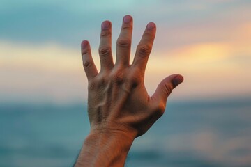 Hand reaching out to touch the sky at sunset.