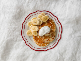 Pancakes with Greek yogurt and banana on a light background, top view. Delicious breakfast