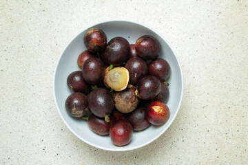 Matoa fruit (Pometia pinnata) typical of Papua Indonesia in a white bowl with a terrazzo granite background