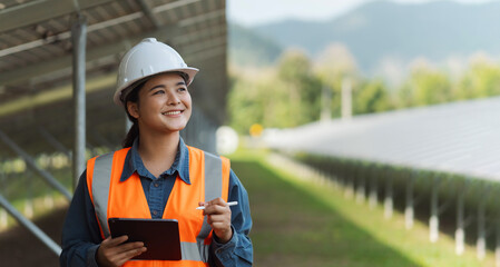 Female electrical engineer wearing hard hat using laptop checking solar panel farm equipment. Eco-friendly energy. Renewable clean energy technology concept. © Dee karen