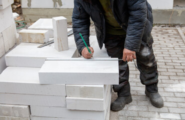 A man is writing on a white brick wall with a pencil