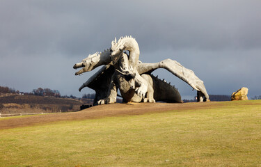 A large dragon statue is standing on a grassy hill