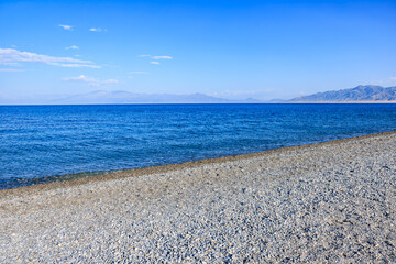 Gravel beach ground and blue lake water natural landscape. Beautiful Sayram Lake scenery in...