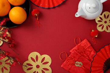 Chinese New Year concept with traditional red envelopes, oranges in a bowl, ornate fans, and a white teapot on a festive red background