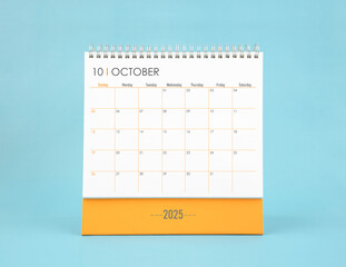 October 2025 white desk calendar on blue color background.