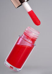Red lip gloss tube and applicator on gray background with shadow.