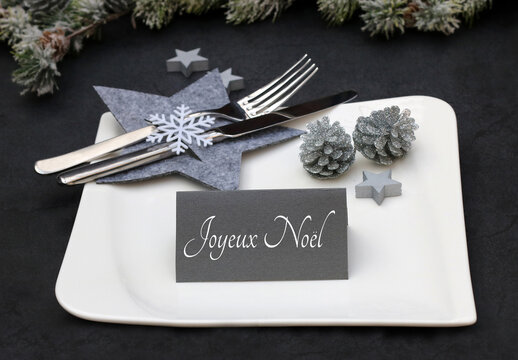 D&eacute;coration de table pour la f&ecirc;te de No&euml;l. Des bougies avec des branches de sapin et une table dress&eacute;e sur un marque-place lit le texte Joyeux No&euml;l.