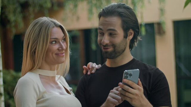 The couple stands outside, tapping their smartphone screen. They win a prize on a mobile app and turn the green screen toward the camera, highlighting the victory and enjoying their sudden success.