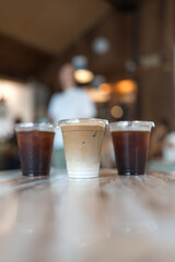 Close up view a glass of ice latte placed on the center between ice black coffee, desk blurred background, drink beverage