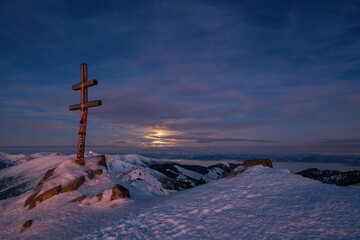 Dumbier Low Tatras, Winter mountain landscape illuminated by the moon. Hill top with snow and cross, night sky with moon. Discover the beauty of winter nature walks.