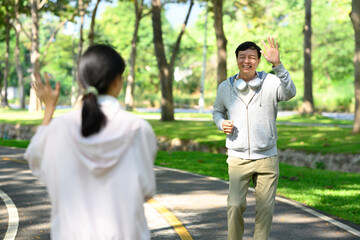 Cheerful senior man greeting a friend during jogging in the park