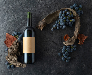 Bottle of red wine, blue grapes, and old vine snags on a black stone background.