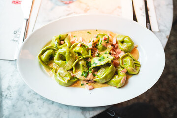 Delicious Spinach Tortellini Pasta Dish Served on a White Plate with Creamy Sauce and Ham Pieces, Topped with Fresh Parsley For an Authentic Italian Culinary Experience at a Restaurant