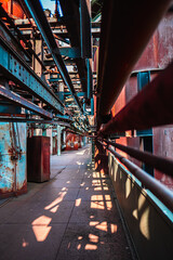 Intricate Industrial Factory Interior with Pipes Casting Geometric Shadows on the Ground Pathway Under a Bright Blue Sky