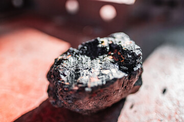 Close-Up of Shiny Coal Nugget on Red Surface Highlighting Its Rich Black Mineral Texture and Industrial Value in a Natural Resource or Mining Context