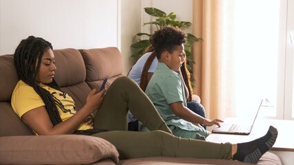 Woman using smartphone while brother and mother using laptop at home