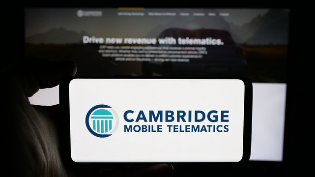 Stuttgart, Germany - 11-15-2024: Person holding cellphone with logo of US company Cambridge Mobile Telematics Inc. (CMT) on screen in front of webpage. Focus on phone display.