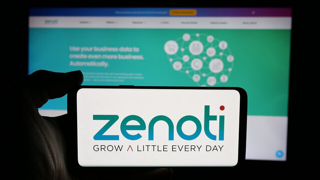 Stuttgart, Germany - 11-15-2024: Person holding cellphone with logo of US salon software company Soham Inc. (Zenoti) on screen in front of business webpage. Focus on phone display.