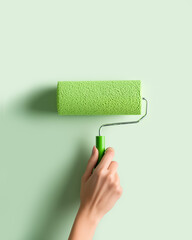 Obraz premium Woman paints wall with paint roller loaded with pastel green color, isolated background. Diy creative concept of renewal, rejuvenation, personalization, transformation of interior.