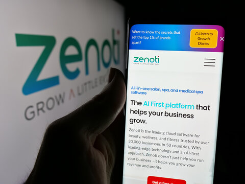 Stuttgart, Germany - 11-15-2024: Person holding mobile phone with website of US salon software company Soham Inc. (Zenoti) on screen with logo. Focus on center of phone display.
