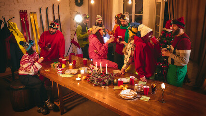 Holiday joy radiates as friends dressed in ski-themed winter clothes toast with red cups, surrounded by string lights, decorated table, and festive ornaments. Concept of travel, Christmas party. Ad