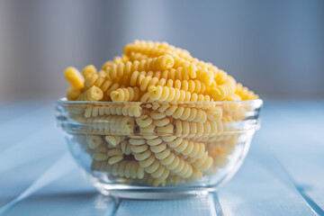 Uncooked italian pasta. Fusilli pasta in bowl on blue table.