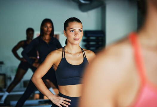 Fit young woman in sportswear standing with her hands on her hips on a reformer during a women's pilates class in a gym