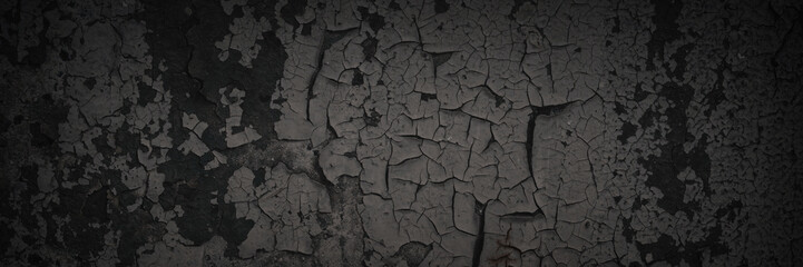Dark wide panoramic background. Peeling paint on a concrete wall. Dark grunge texture of old cracked flaking paint. Weathered rough painted surface. Patterns of cracks. Darkness background for design.
