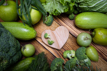 Frame of green vegetables and a heart on wooden background