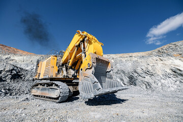Big yellow Excavator working in Open Pit Mine Under Clear Blue Sky.