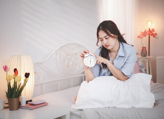 An Asian woman wakes up in the morning and sits on her bed with an alarm clock. She doesn't want to...