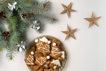 Christmas tree branch with decorations and plate with gingerbread on white background. Flat lay, top view.