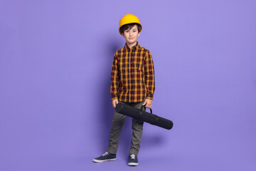 Boy with blueprint tube pretending to be architect on violet background. Dreaming of future profession