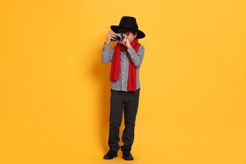 Boy with camera pretending to be photographer on orange background. Dreaming of future profession