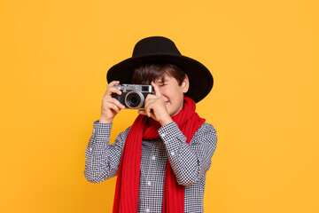 Boy with camera pretending to be photographer on orange background. Dreaming of future profession