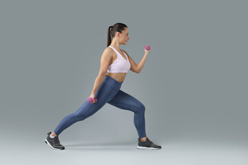 Woman exercising with dumbbells on light grey background, space for text